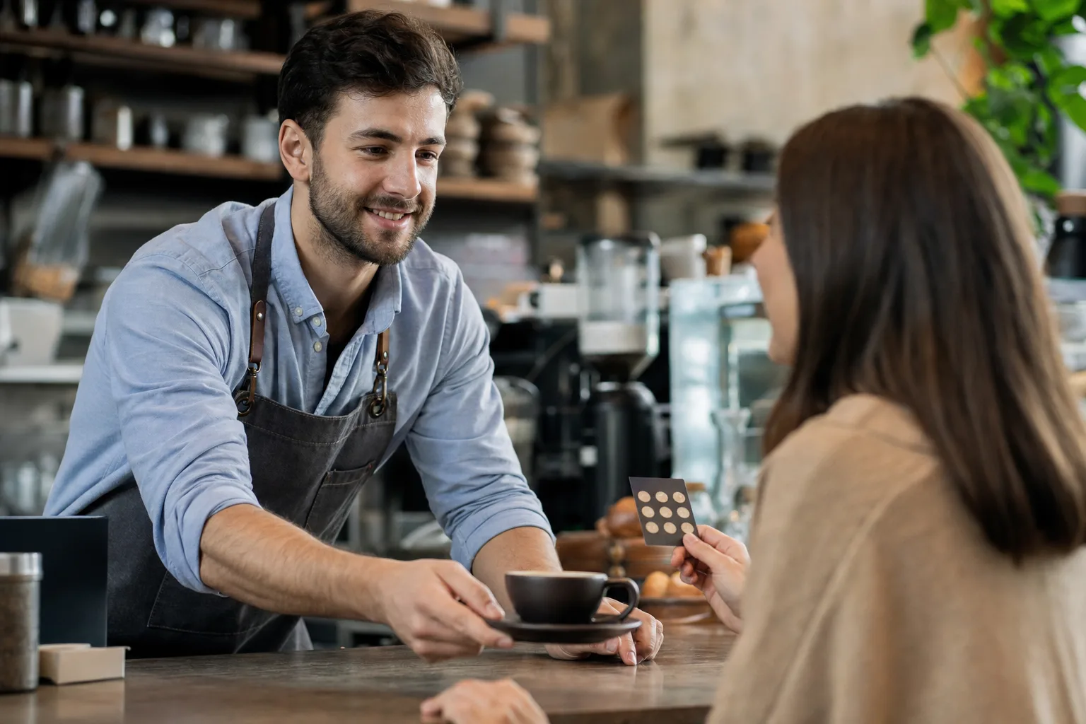 barista kávét készít törzsvendégnek egy hangulatos kávézóban, ahol a vendég egy pontgyűjtő kártyát tart a kezében
