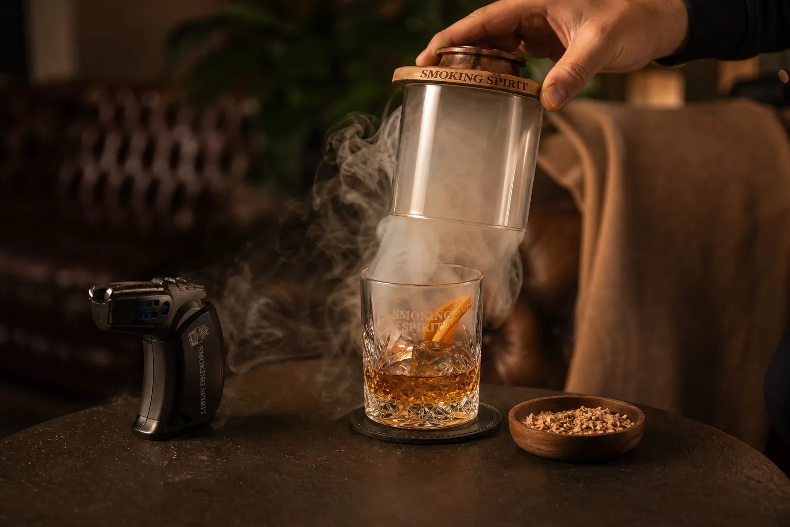 Otthoni nappali félhomályban: egy alacsony dohányzóasztalon jéggel teli whiskys pohár áll narancshéjjal, a pohár fölött üvegkupola alatt sűrű füst kavarog, mellette kis füstölőpisztoly és egy tálkában faforgács; egy kéz éppen felemeli a kupola szélét, hogy a füst kiáramoljon.