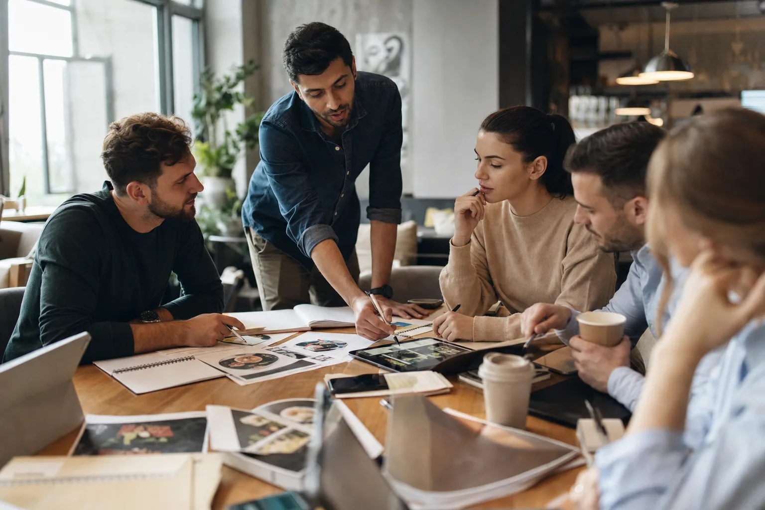 marketing csapat brainstormingol egy nagy asztalnál, digitális eszközök használatával