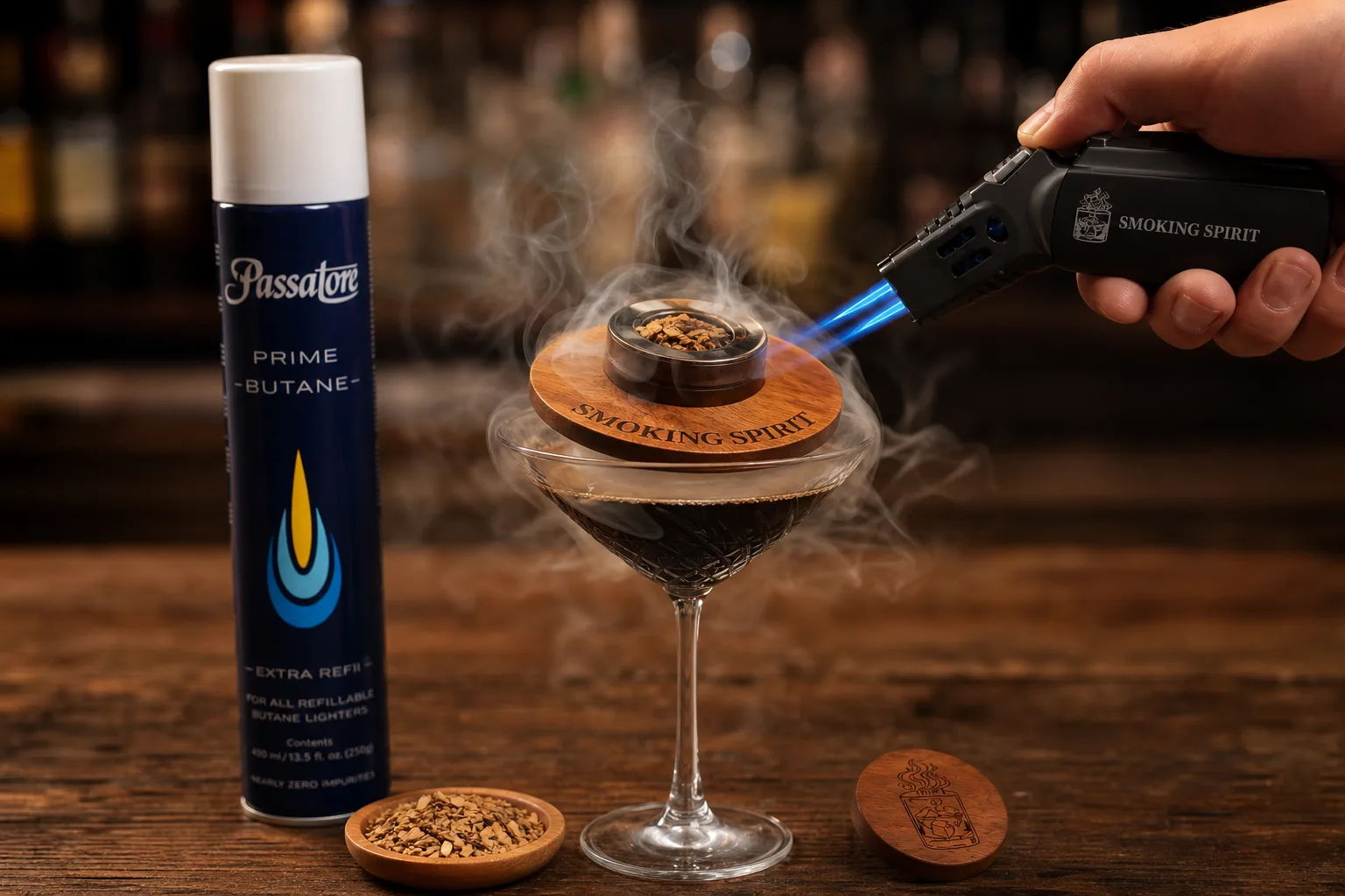 Sötét fa bárpulton whiskey füstölő szett fa fedővel egy espresso martinis pohár tetején, mellette kis tálkában faforgács és kézi fáklya; egy kéz épp meggyújtja a forgácsot, a füst leereszkedik a pohár köré.